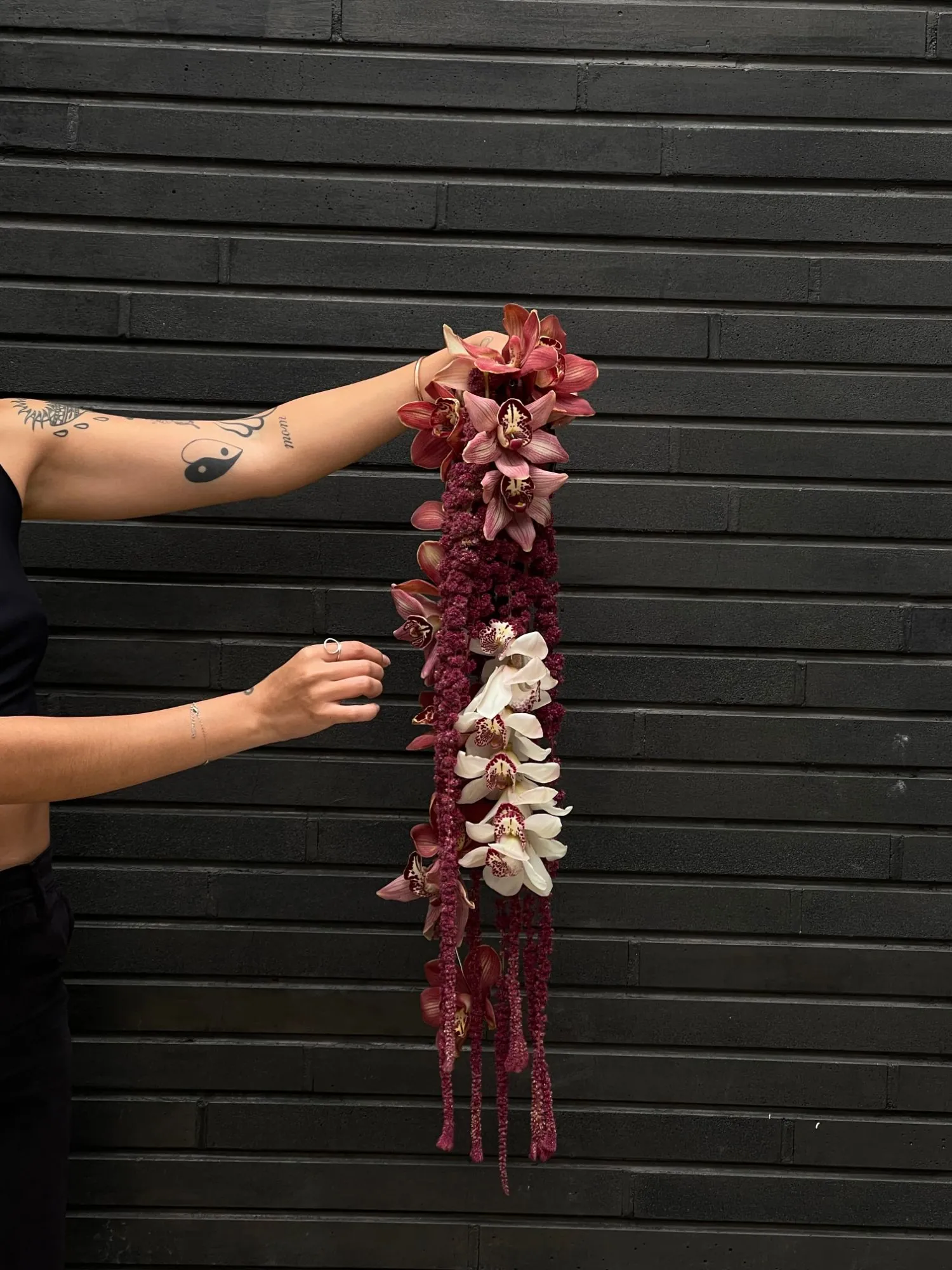 Cascada de orquídeas cymbidium y amaranto sostenida contra un muro negro